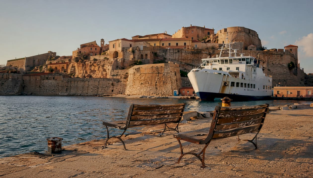 Il porto di Portoferraio al tramonto, con il traghetto in arrivo e le antiche fortezze medicee illuminate dalla luce dorata della sera.