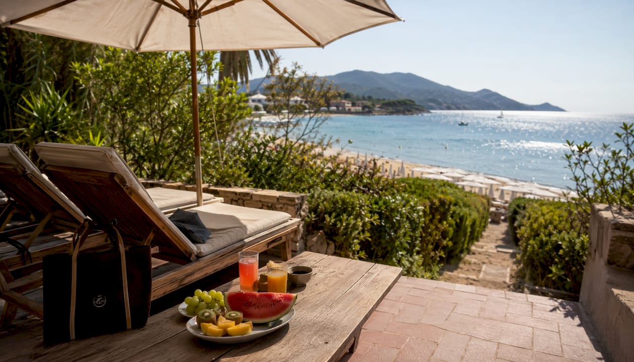 Una terrazza panoramica di un hotel sul Mediterraneo, con vista sulla spiaggia dove una famiglia si gode il sole e il mare.